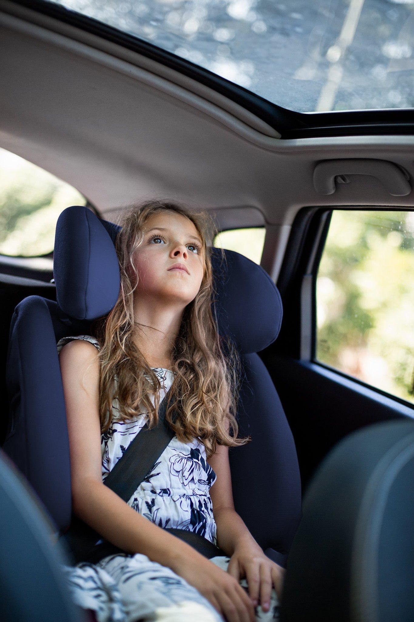 Dziewczynka w sukience siedzi w foteliku samochodowym